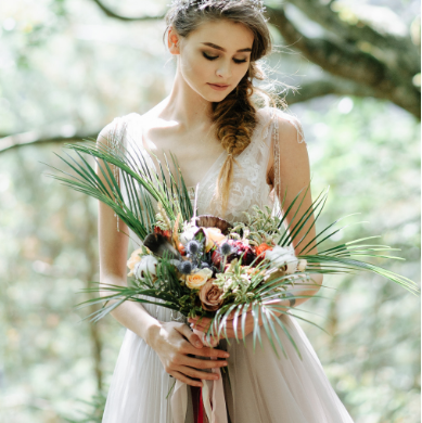 A young bride holding a bouquet of tropical flowers and palm fronds